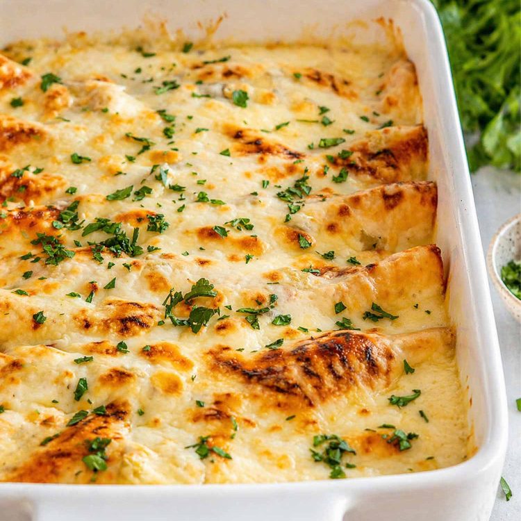 Golden bubbly mozzarella cheese over white chicken enchiladas in a white baking dish garnished with fresh chopped green cilantro.
