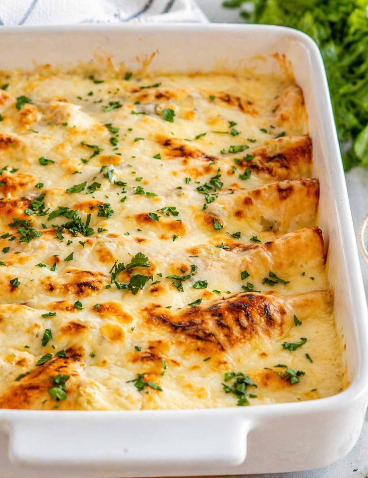 Golden bubbly mozzarella cheese over white chicken enchiladas in a white baking dish garnished with fresh chopped green cilantro.