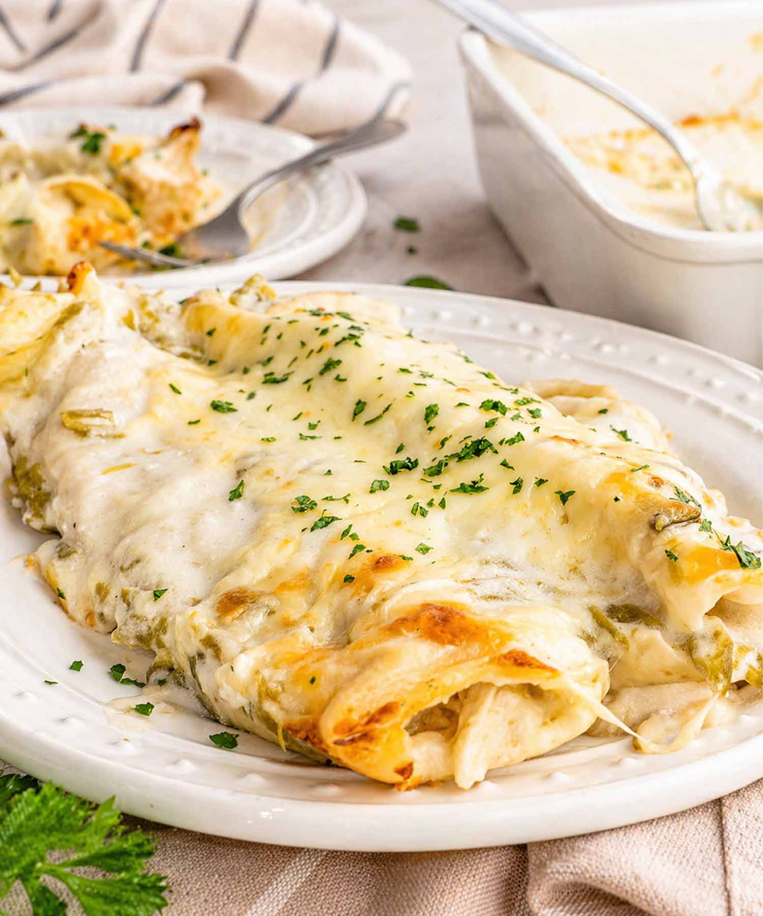 Close up of creamy white chicken enchiladas on a white plate showing melted cheese and smooth green chile sauce.