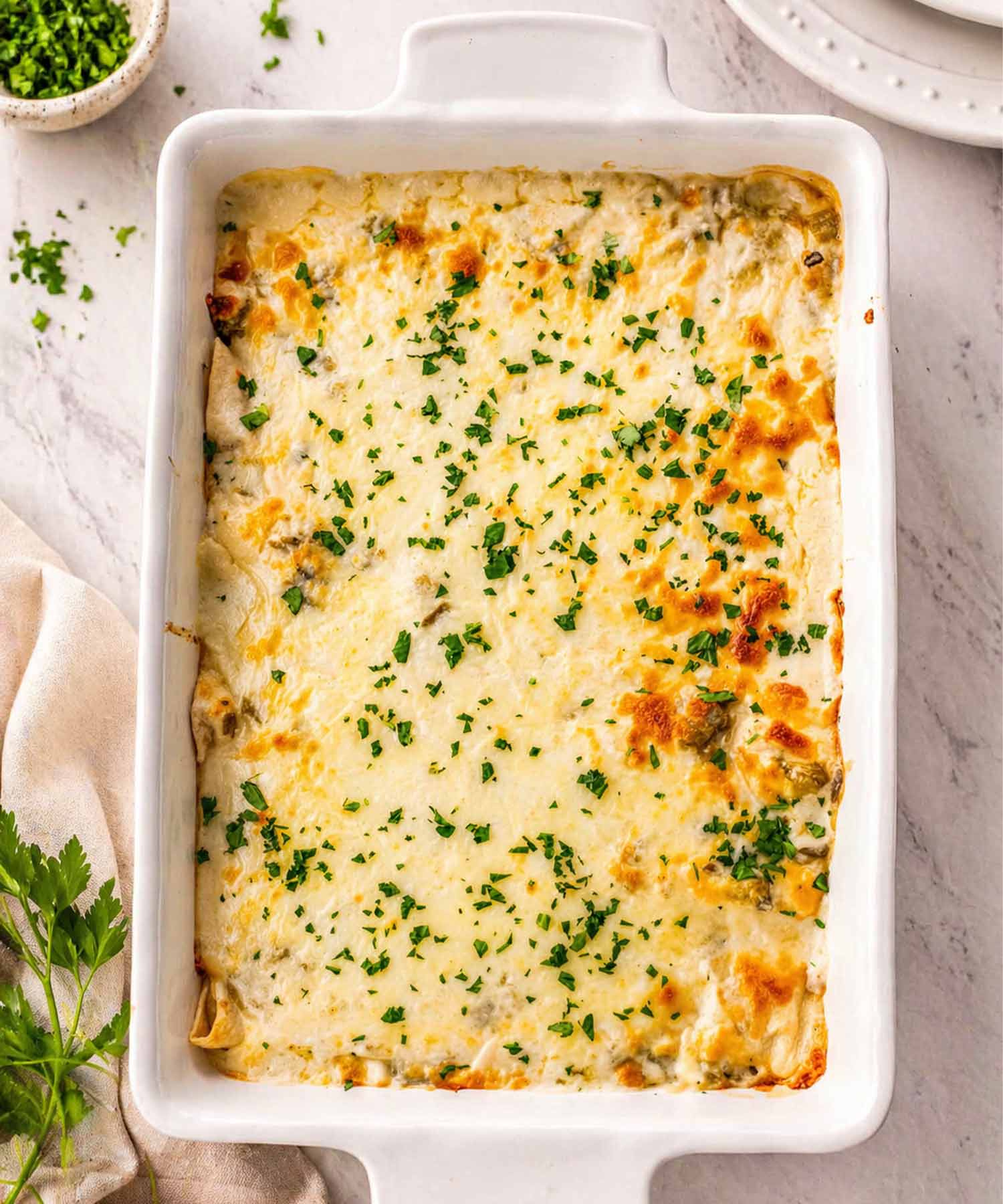 Overhead view of a 9x13 baking dish filled with six flour tortilla chicken enchiladas smothered in creamy white sauce.