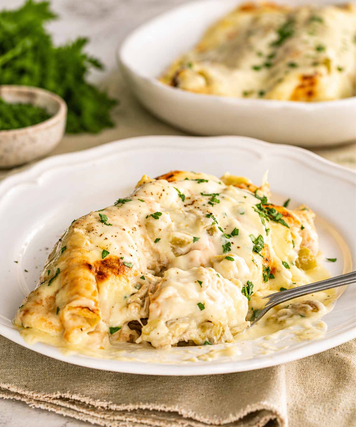 A single serving of cheesy white chicken enchilada being lifted with a fork to show the creamy sauce texture.