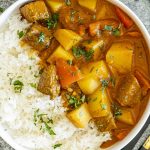 Overhead view of beef and potato curry served with rice in a white bowl, garnished with fresh chopped cilantro.