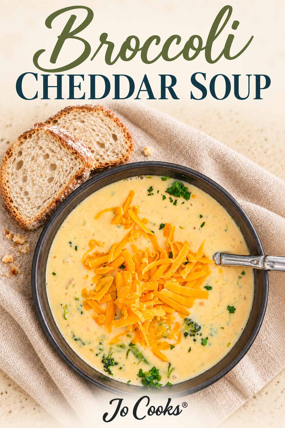 Broccoli cheddar soup in a dark bowl beside sliced bread, with recipe title above and Jo Cooks logo below.