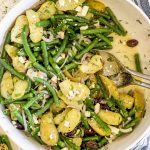 Overhead shot of large mixing bowl filled with lemony potato and green bean salad topped with crumbled feta.