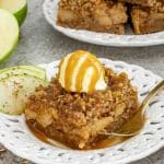 Slice of caramel apple crisp bar topped with vanilla ice cream and caramel drizzle, served with fresh apple slices.