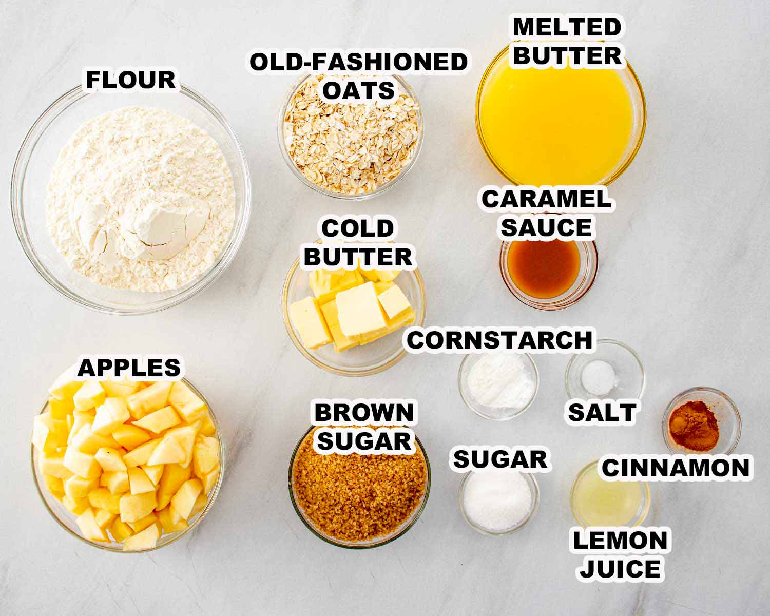 Overhead view of measured ingredients for caramel apple crisp bars, including apples, oats, flour, sugar, butter, and caramel.