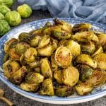 Close-up of crispy Maple Dijon Roasted Brussels Sprouts coated in a sweet and tangy glaze served in a patterned blue bowl.