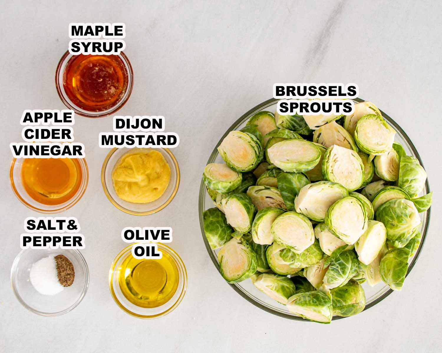 Overhead view of trimmed Brussels sprouts with maple syrup, Dijon mustard, apple cider vinegar, olive oil, salt and pepper, showing everything needed for Maple Dijon Roasted Brussels Sprouts.