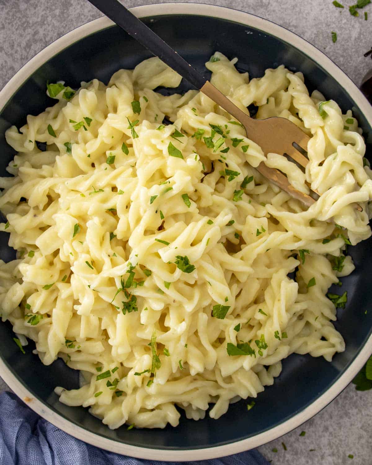 Creamy cafeteria noodles coated in chicken broth and soup, sprinkled with parsley, served in a bowl with a fork.