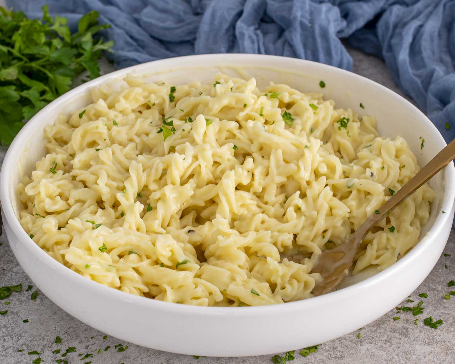 Smooth and creamy cafeteria noodles in a white serving bowl, tossed with butter and soup, sprinkled with fresh parsley.