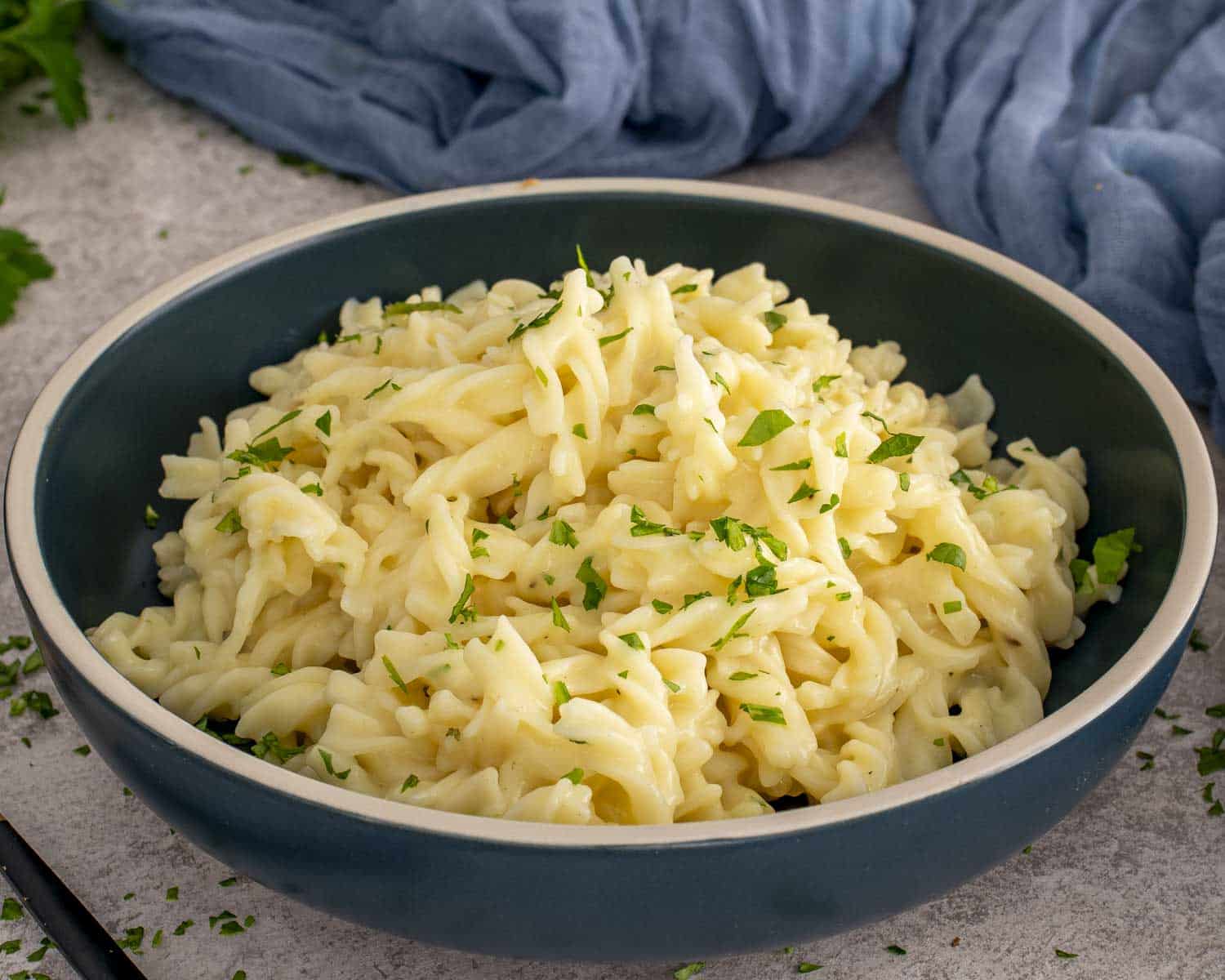 Creamy egg noodles served in a deep bowl, finished with chopped parsley and black pepper for a cozy, simple side.