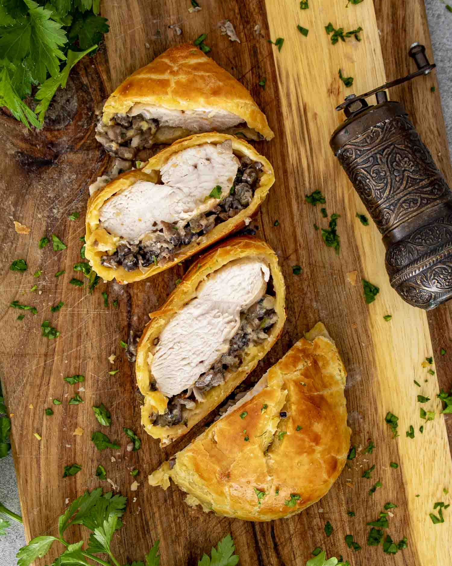 Chicken Wellington sliced on a wooden board, showing golden pastry, tender chicken, and finely chopped mushroom filling.