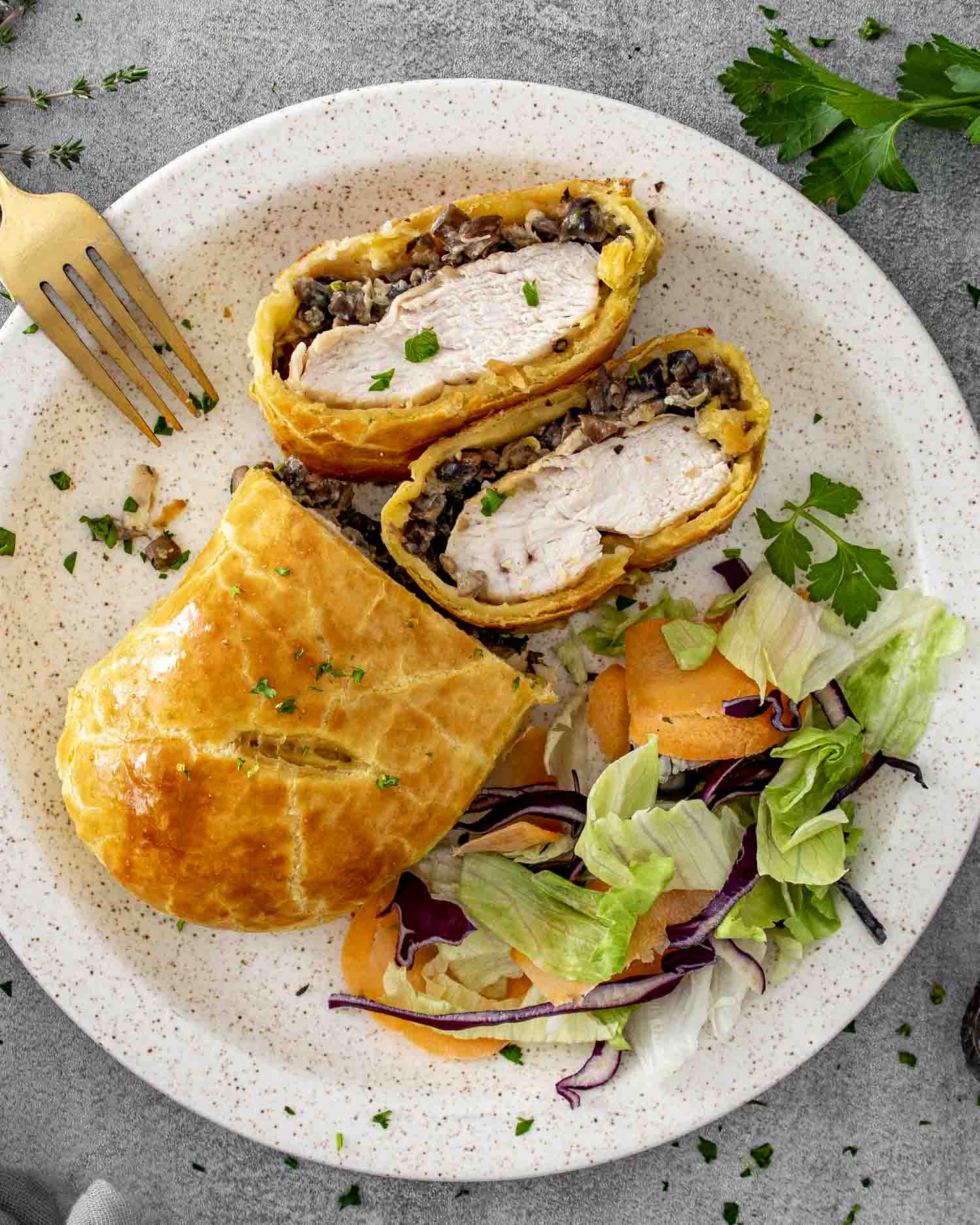 Overhead view of Chicken Wellington slices on a plate with salad, highlighting flaky pastry and juicy chicken center.