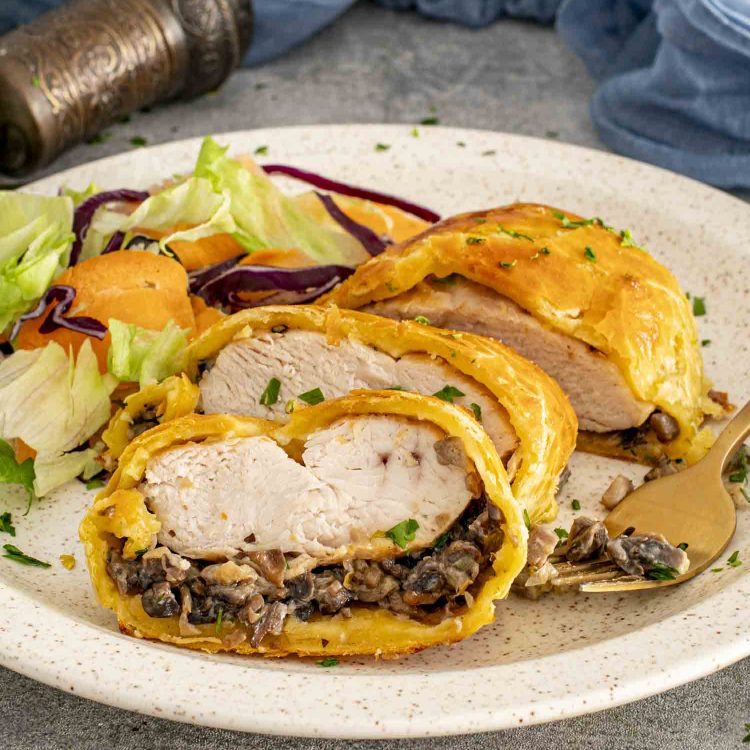 Chicken Wellington slices on a plate with mixed salad, highlighting crisp golden pastry and creamy mushroom duxelles filling.