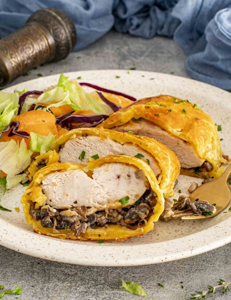 Chicken Wellington slices on a plate with mixed salad, highlighting crisp golden pastry and creamy mushroom duxelles filling.