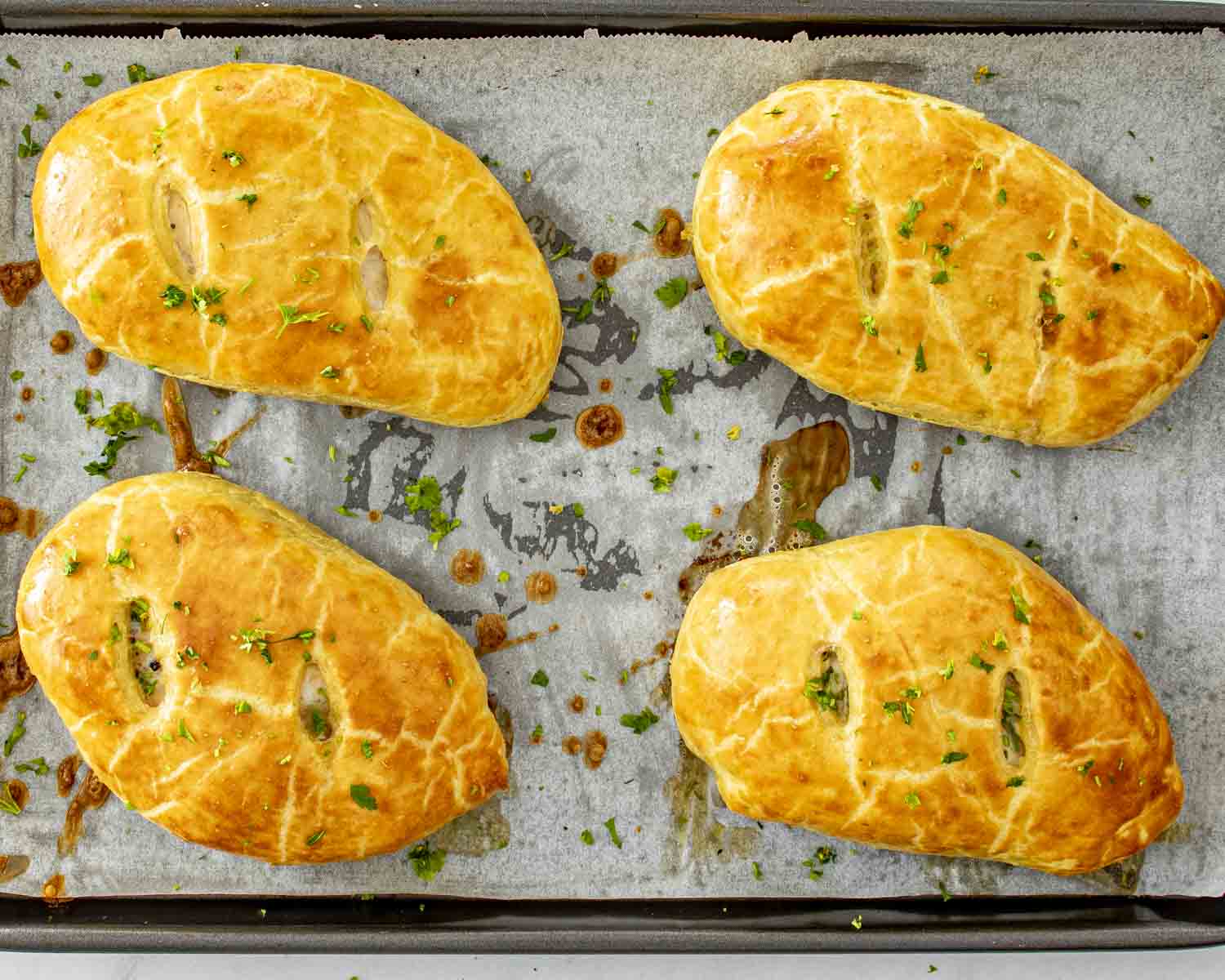 Golden brown chicken Wellingtons resting on a parchment lined baking sheet, garnished with fresh parsley after baking.