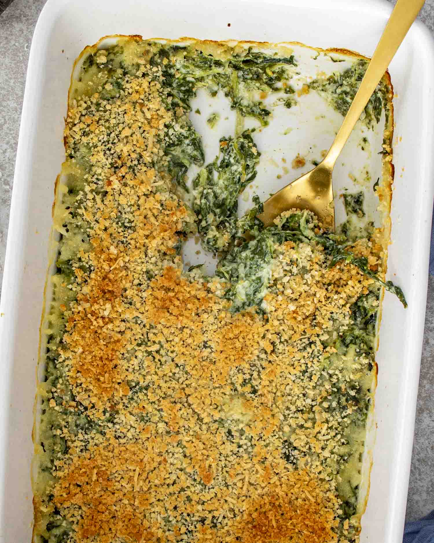 Golden baked spinach gratin in a casserole dish with crunchy breadcrumb topping and creamy spinach visible underneath.
