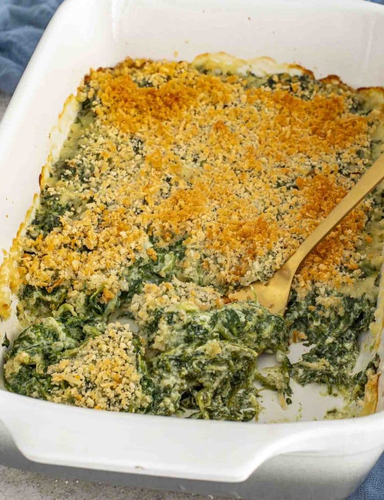 Spinach gratin baked with a crunchy panko topping, shown in a casserole dish with creamy filling being scooped out.