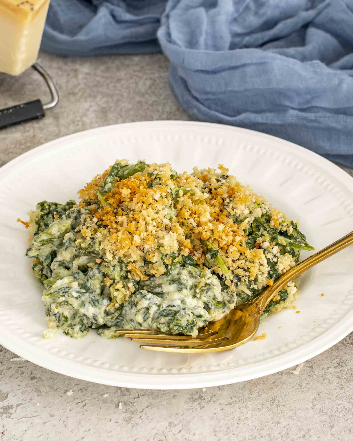 Warm spinach gratin on a white plate topped with crunchy Parmesan breadcrumbs, ready to serve as a holiday side.