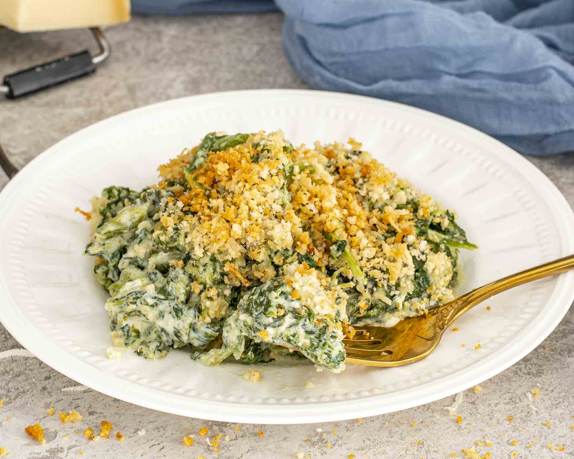 Creamy spinach gratin served on a white plate with a crisp breadcrumb topping and rich cheese sauce.