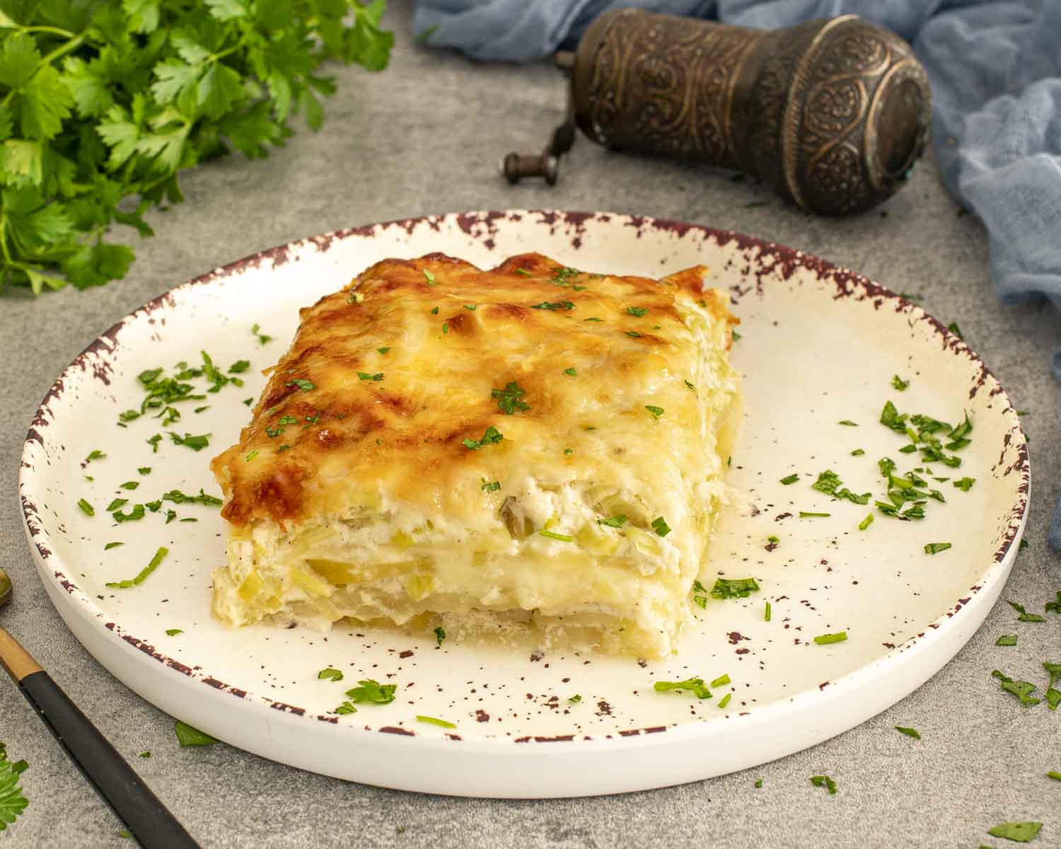 Creamy Gruyère scalloped potatoes with leeks, layered and cheesy, plated and garnished with parsley, fork lifting tender bite.