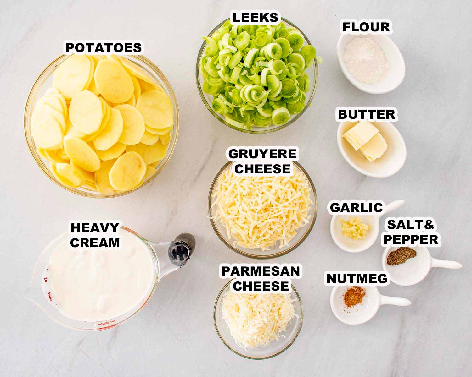 Sliced Yukon Gold potatoes, leeks, Gruy&egrave;re, Parmesan, cream, butter, garlic, flour, nutmeg, salt, and pepper arranged for scalloped potatoes.