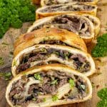 Warm Philly cheesesteak stromboli slices on a wooden board filled with ribeye, onions, peppers, mushrooms, and melted cheese.
