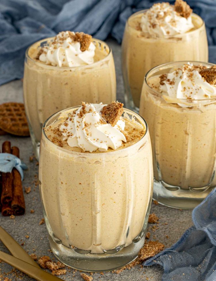Four glasses filled with pumpkin mousse topped with whipped cream and crushed gingersnaps, perfect make ahead fall dessert idea.