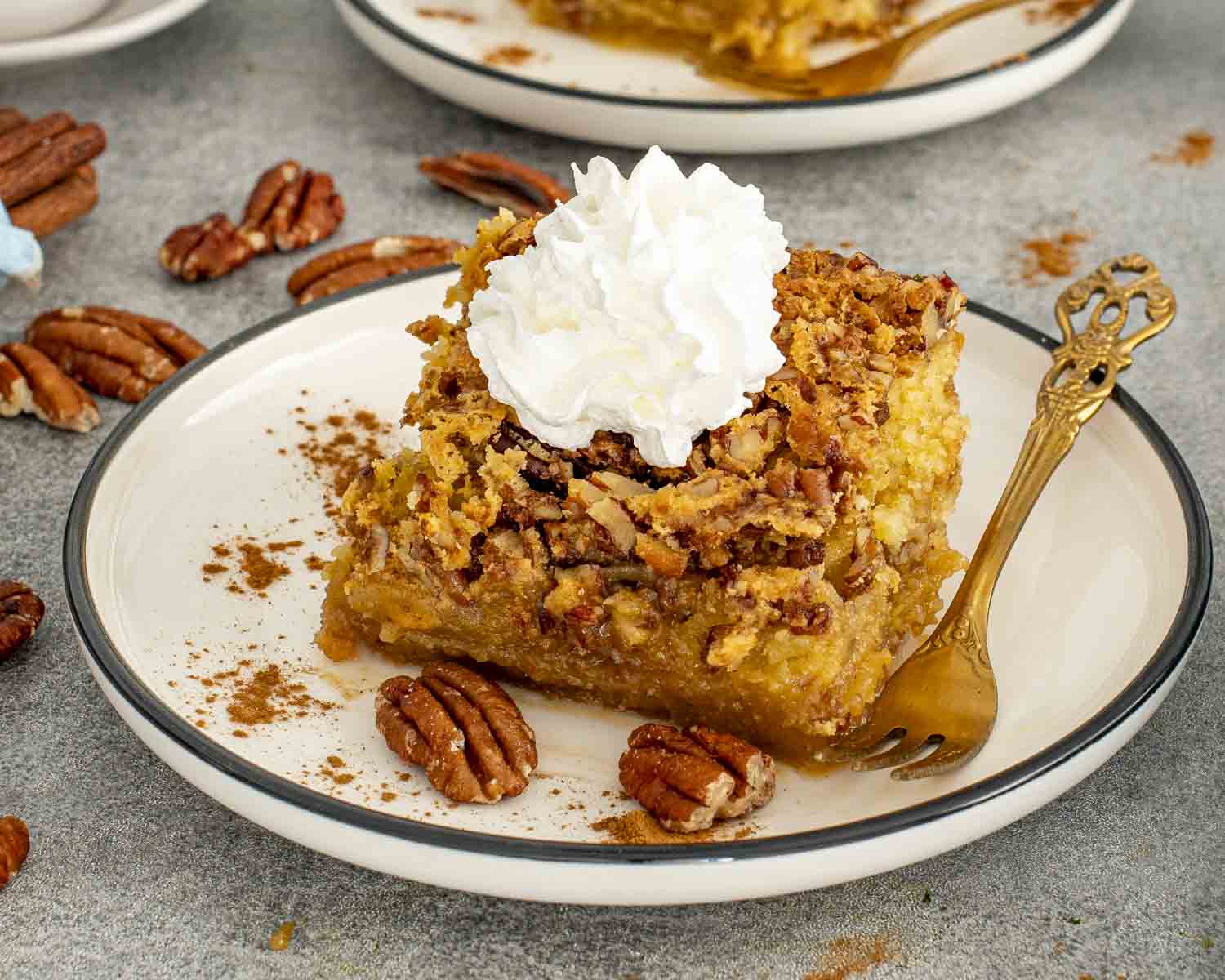 Pumpkin pecan gooey cake square topped with whipped cream and surrounded by pecans and cinnamon on the plate.