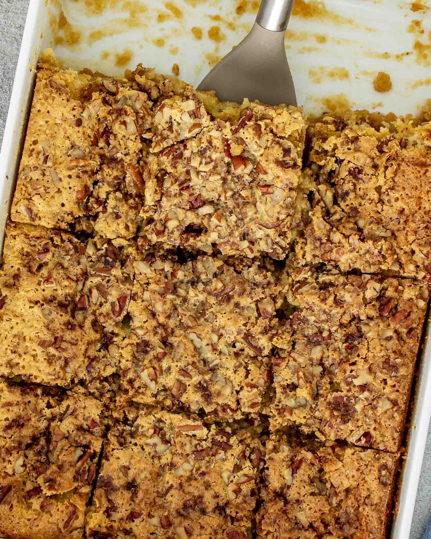 Pumpkin pecan gooey cake cut into squares in a baking dish, showing crunchy pecan topping and soft gooey center.