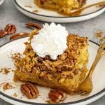 Pumpkin pecan gooey cake slice topped with whipped cream, showing crunchy pecan topping and soft gooey center.