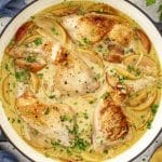 Overhead shot of Chicken Normandy simmering in creamy apple cider sauce with apples, onions, thyme, and golden seared chicken legs.