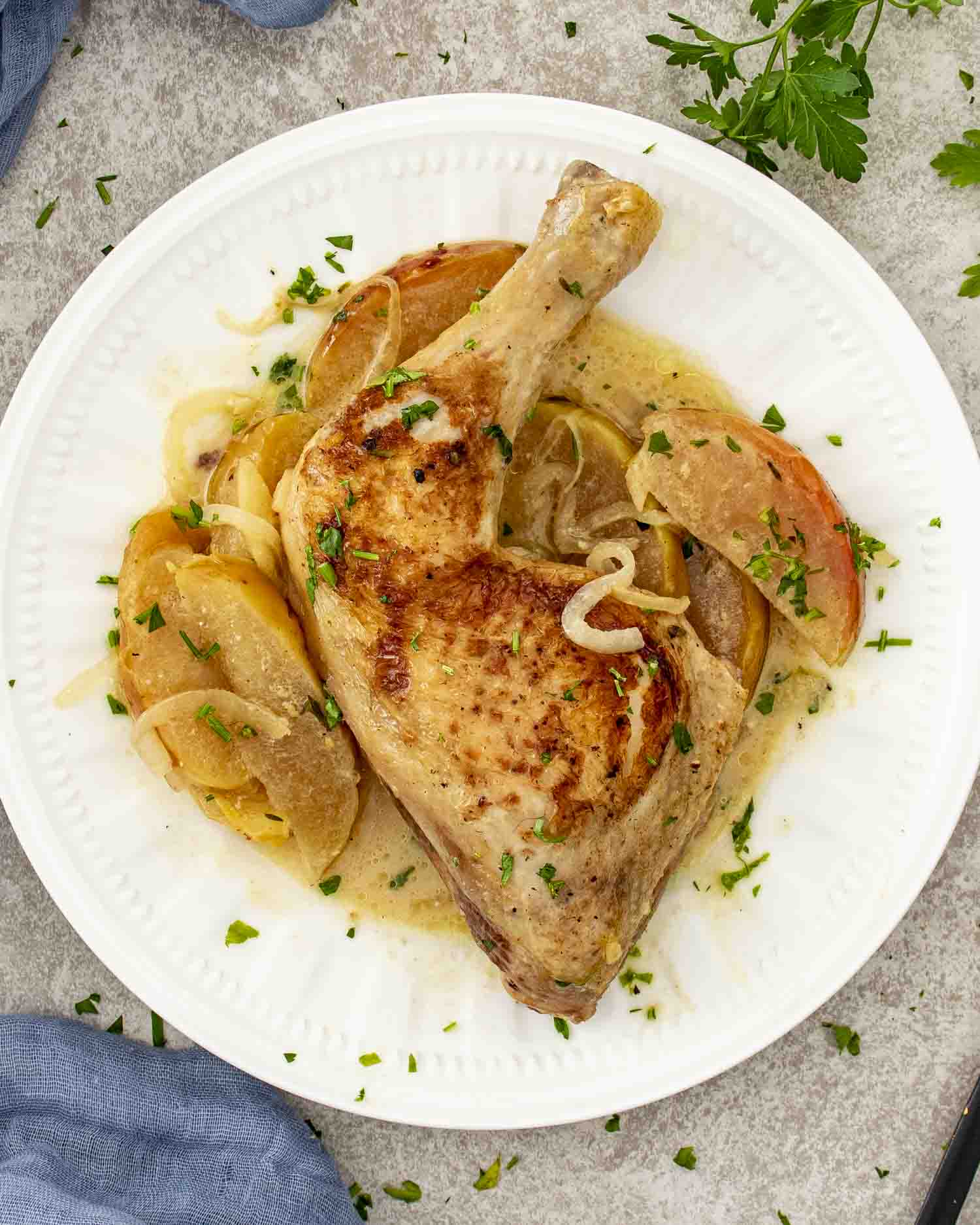 Plated Chicken Normandy featuring a tender braised chicken leg with apples, onions, and creamy cider sauce garnished with parsley.