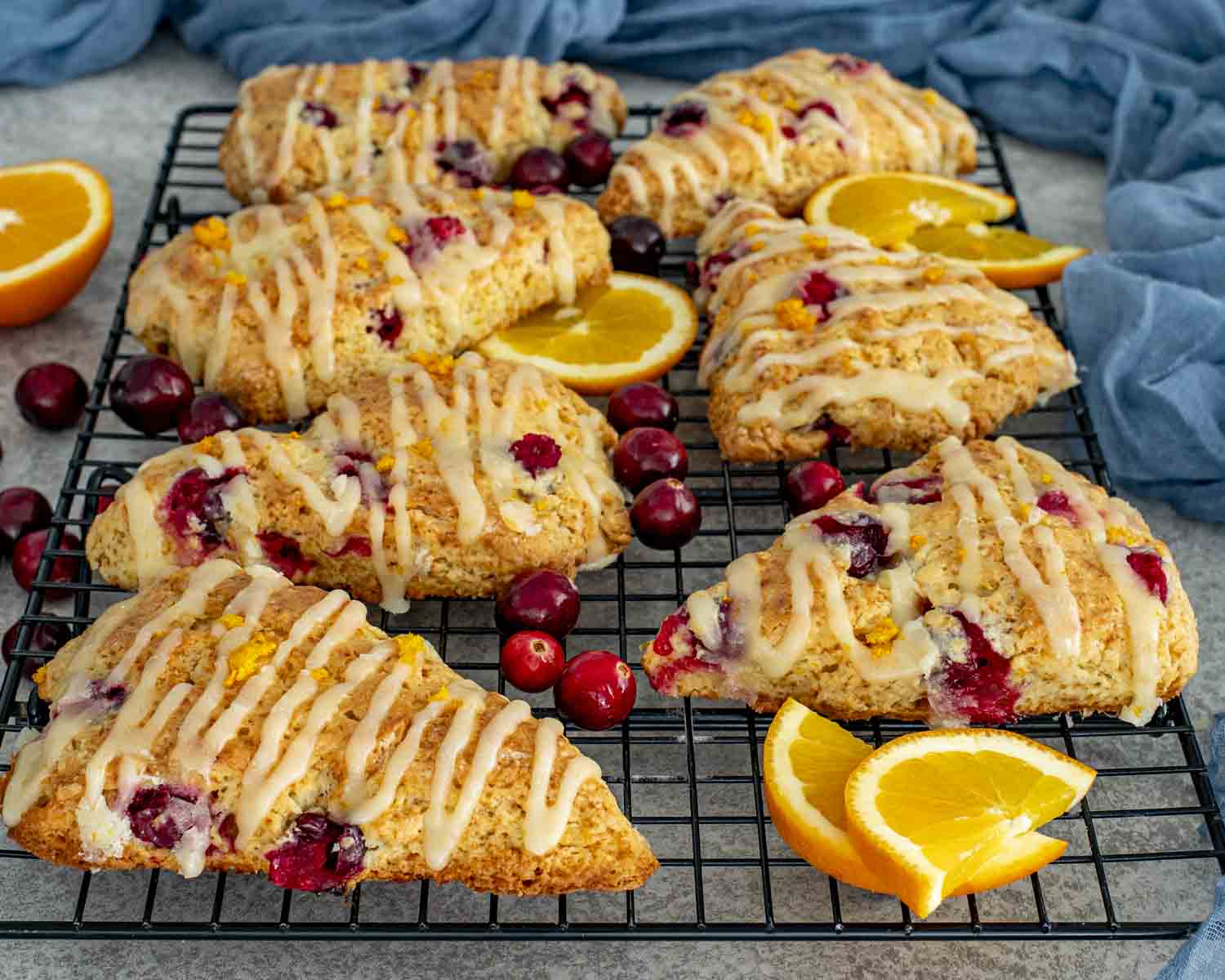 Cranberry orange scones cooling on a wire rack, golden and crumbly with visible cranberries and a generous orange glaze drizzle.