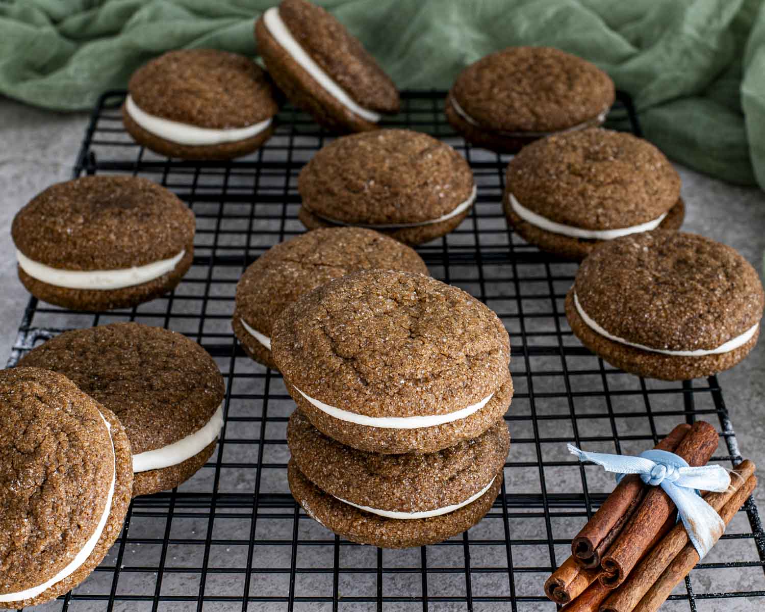 Freshly assembled ginger molasses sandwich cookies resting on a cooling rack with visible cream cheese filling.
