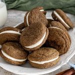 Plate of ginger molasses sandwich cookies with cream cheese filling, showcasing crackled tops and soft, chewy texture.