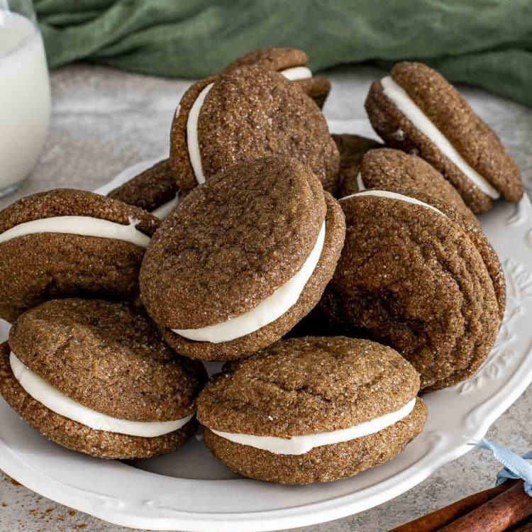 Plate of ginger molasses sandwich cookies with cream cheese filling, showcasing crackled tops and soft, chewy texture.