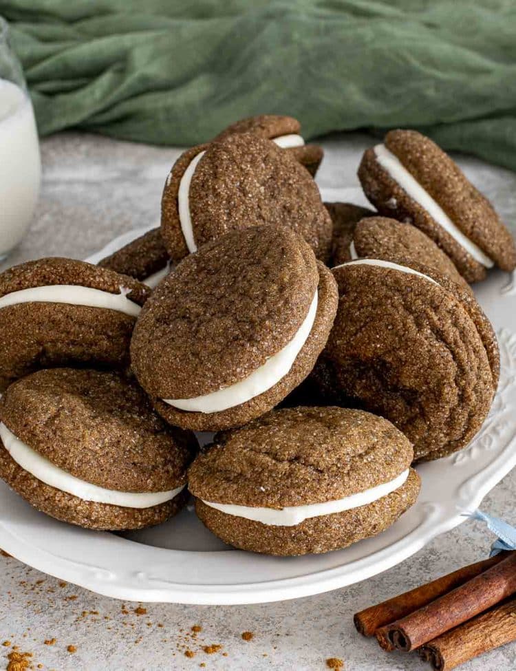 Plate of ginger molasses sandwich cookies with cream cheese filling, showcasing crackled tops and soft, chewy texture.