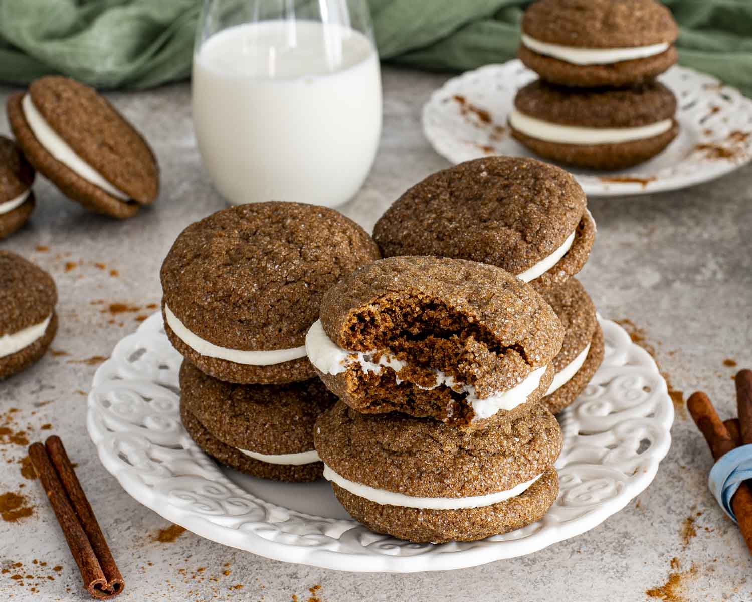 Bitten ginger molasses sandwich cookie revealing soft, chewy interior and creamy filling on decorative serving plate.