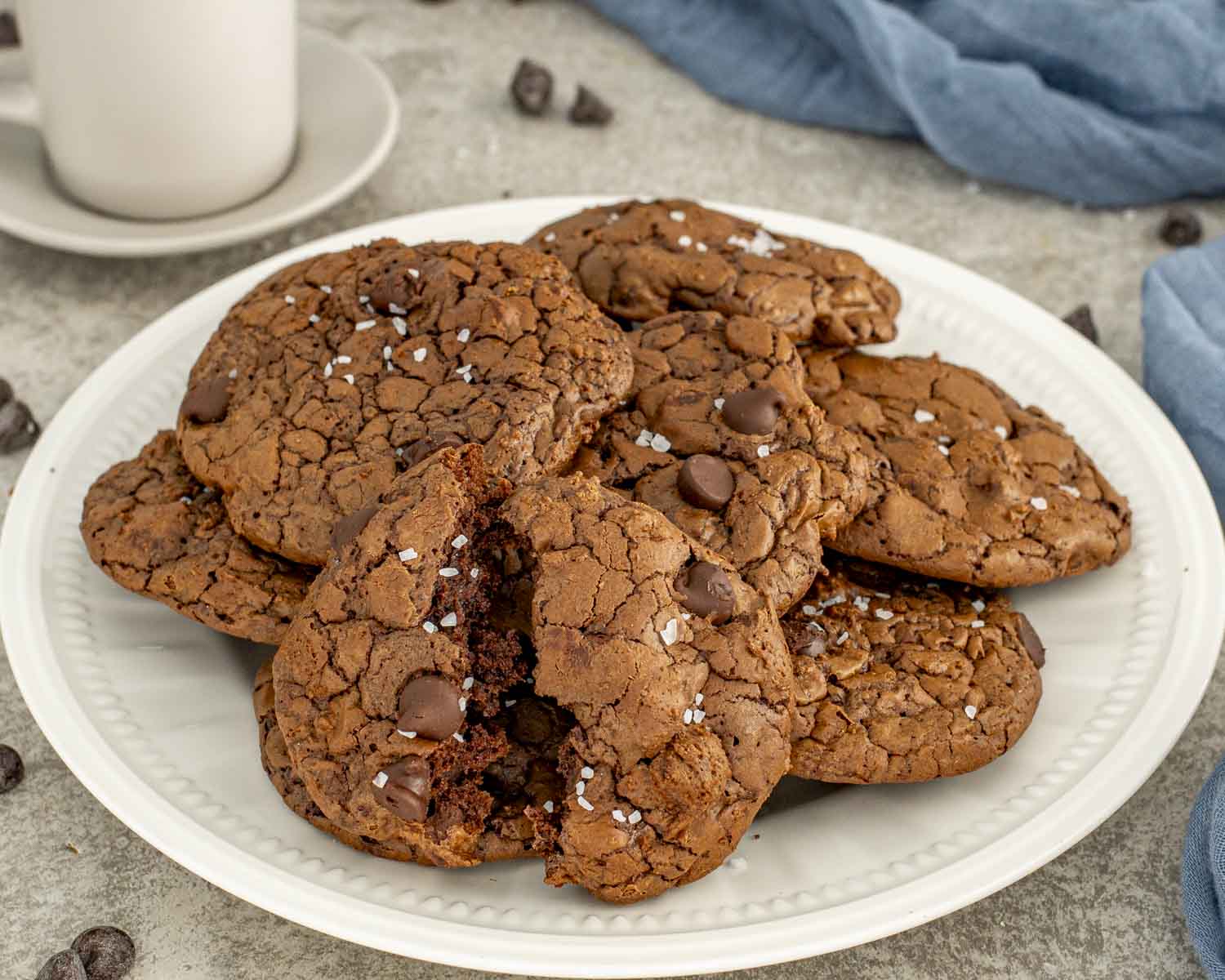 Mocha fudge cookies on a white plate with one broken open, revealing rich fudgy centers and sprinkled with flaky salt.