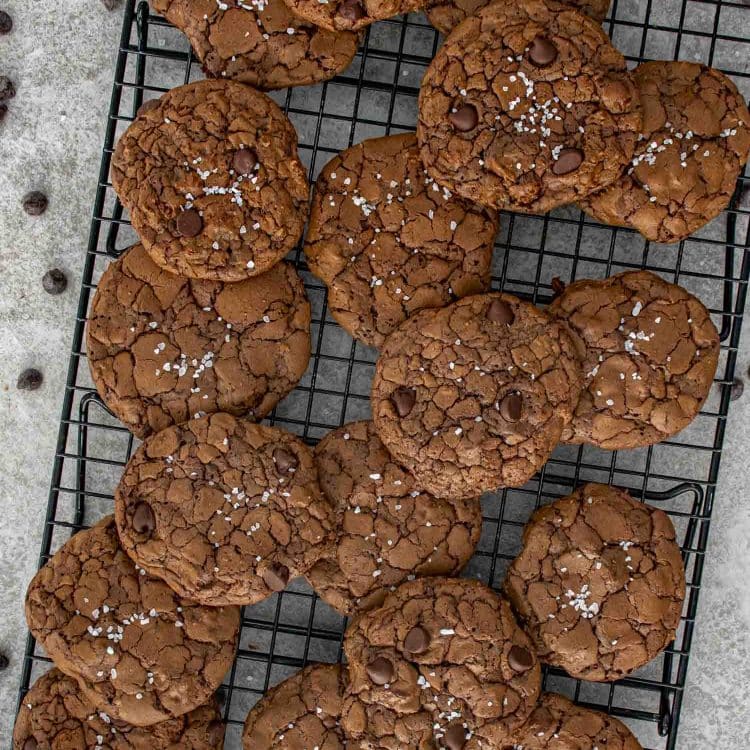 Overhead view of mocha fudge cookies cooling on a wire rack, with crackly surfaces, chocolate chips, and flaky salt garnish.