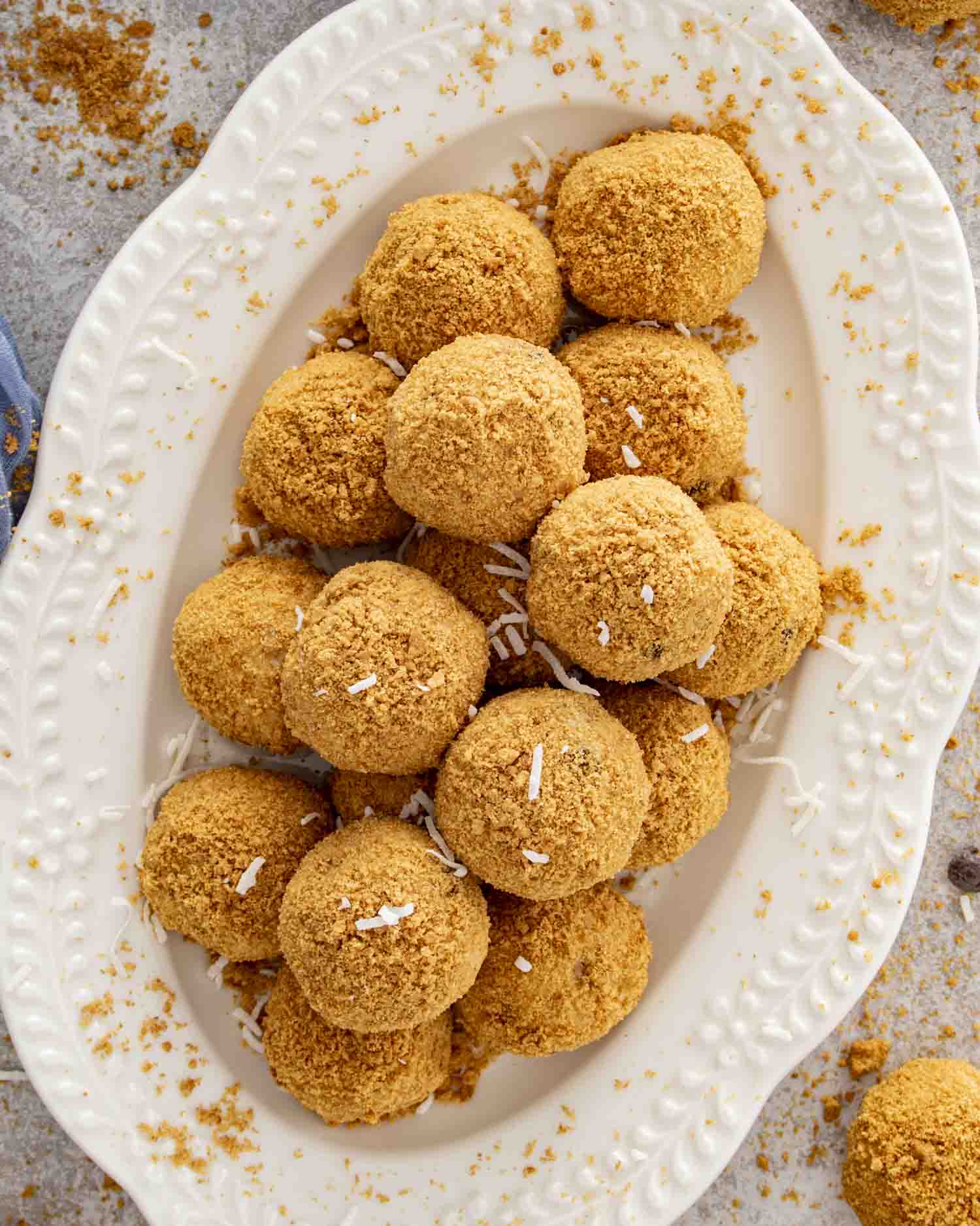 Overhead view of golden graham-covered Moose Farts on a white platter with scattered crumbs and coconut for texture.