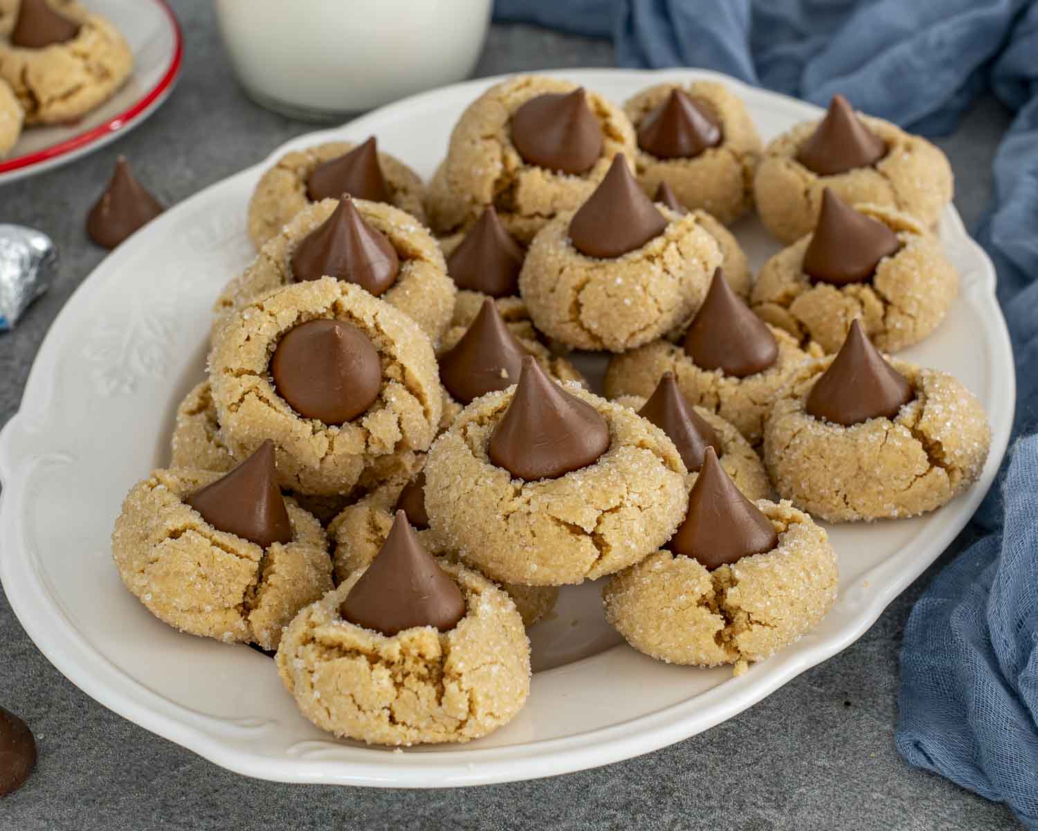 Generous platter of classic peanut butter blossom cookies with sparkly sugar coating and signature chocolate kiss on top of each cookie.