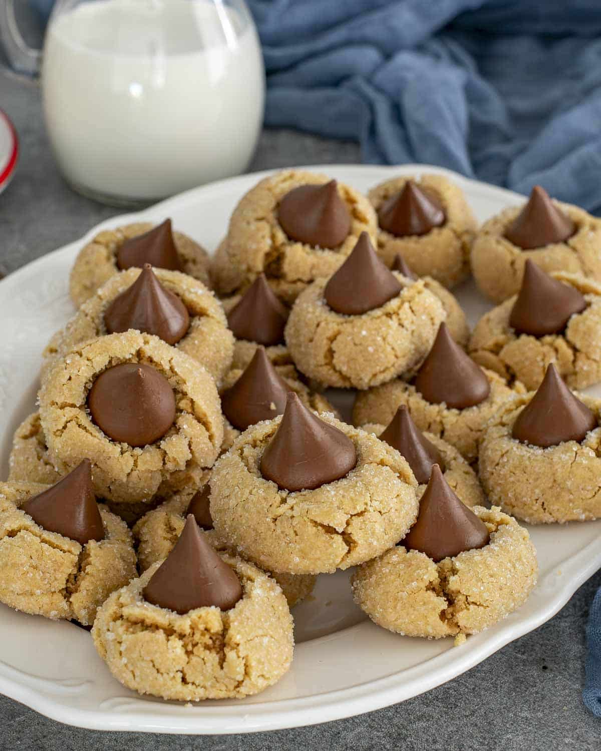 Generous platter of classic peanut butter blossom cookies with sparkly sugar coating and signature chocolate kiss on top of each cookie.