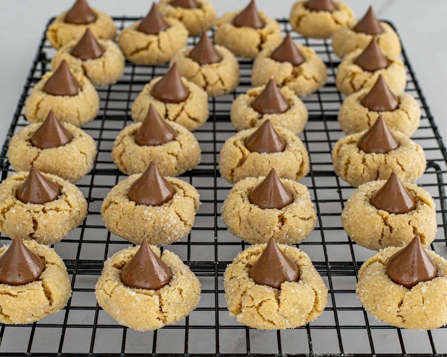 Neatly arranged peanut butter blossom cookies cooling on a wire rack, showing even shape, sugar coating, and chocolate kiss centers.