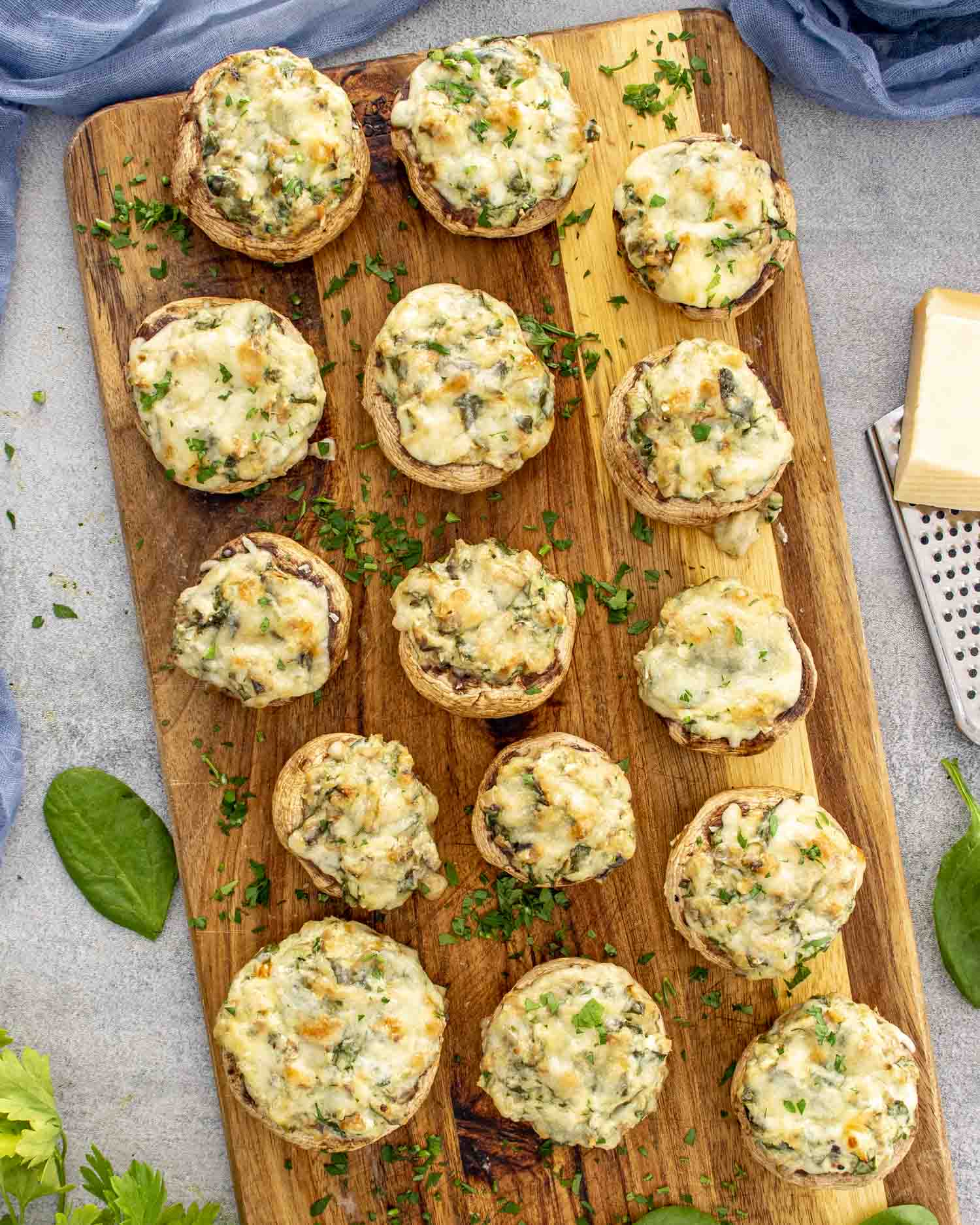 Spinach dip stuffed mushrooms served on a wooden board, melted cheese bubbling slightly over tender roasted mushroom caps.