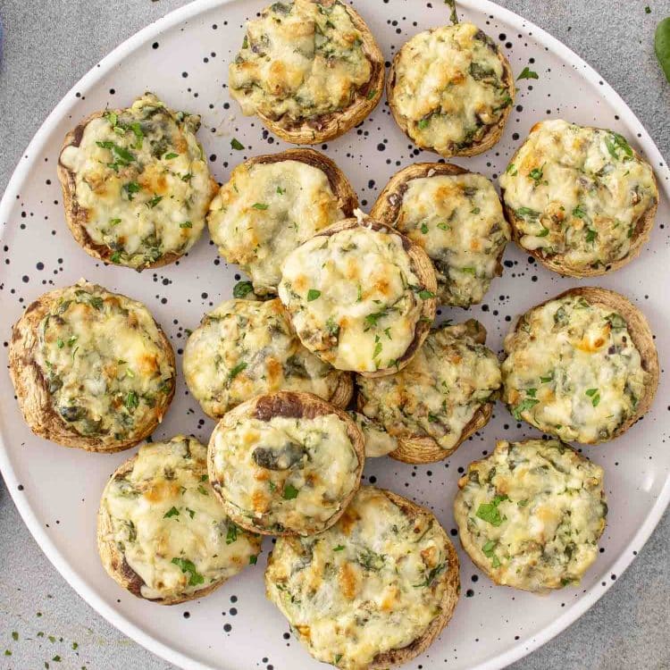 Overhead view of spinach dip stuffed mushrooms arranged on a serving platter, showing creamy filling and lightly browned cheese tops.