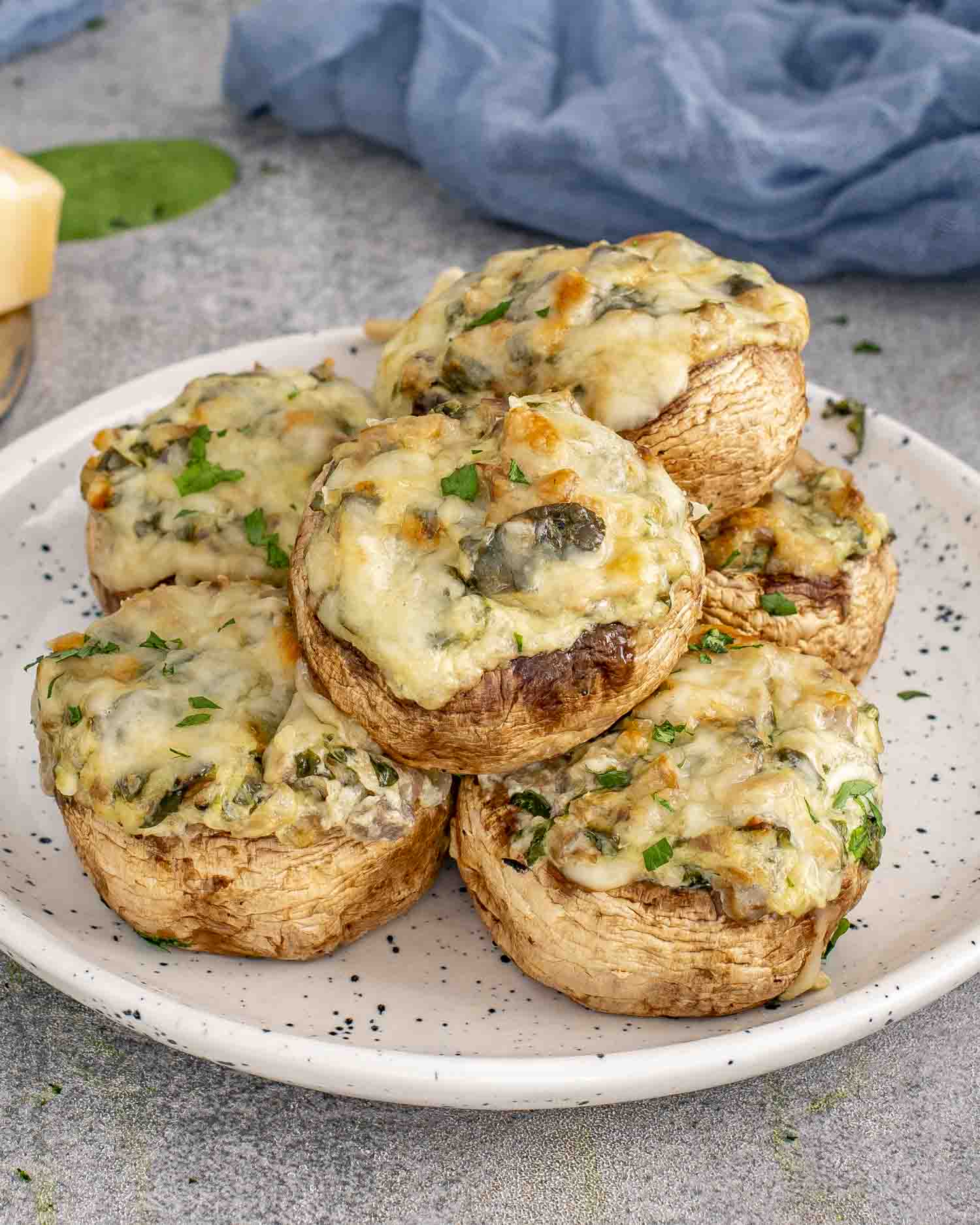 Spinach dip stuffed mushrooms stacked on a plate, baked until golden with melted cheese and sprinkled with fresh parsley.