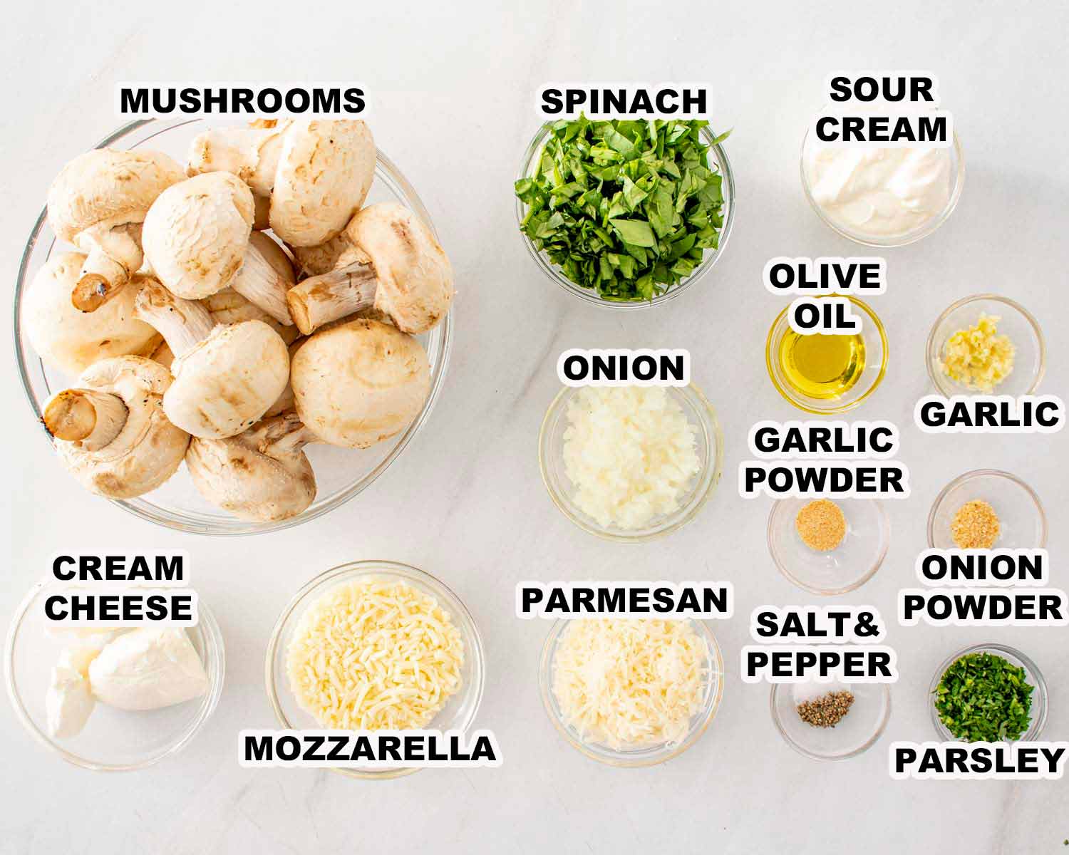 Ingredients for spinach dip stuffed mushrooms including mushrooms, spinach, cream cheese, sour cream, cheeses, garlic, onion, and seasonings.