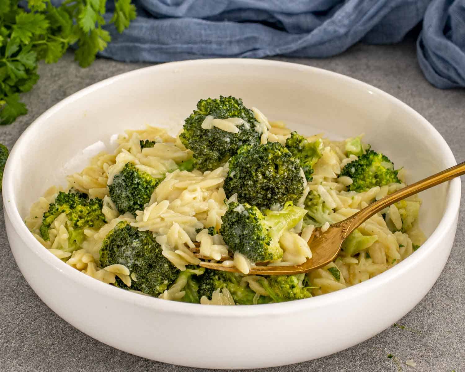 Close-up of broccoli cheddar orzo in a bowl with a fork lifting cheesy orzo and bright green broccoli.